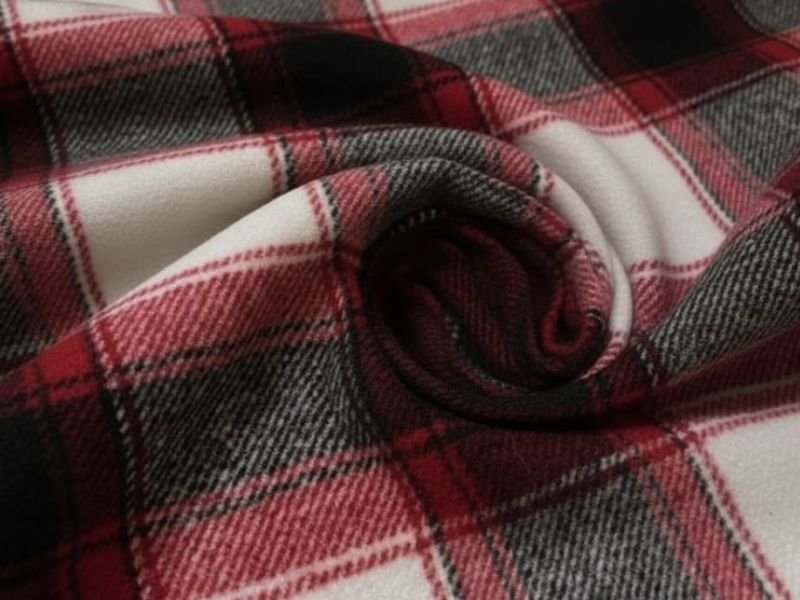 Καρό ύφασμα, μάλλινο, σε αποχρώσεις του κόκκινου, λευκού και μαύρου, διπλωμένο σε απαλές πτυχές.